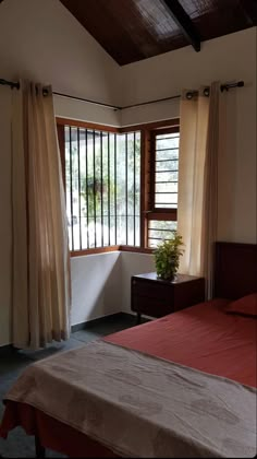 a bed sitting under a window next to a wooden table with a potted plant on it