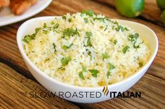 a bowl filled with rice and garnished with parsley next to limes