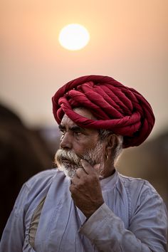 a man with a red turban on his head standing in front of the sun