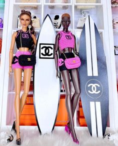 two barbie dolls are standing next to a surfboard