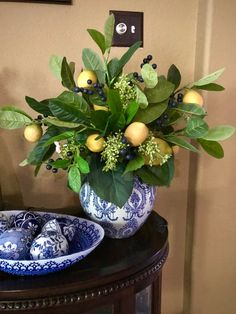 a blue and white bowl with oranges in it sitting on a table next to a vase