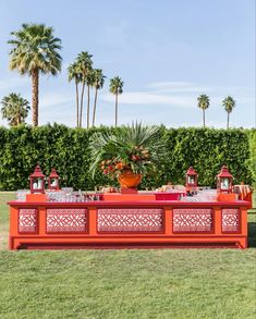 an orange table with drinks on it in the middle of a grassy area surrounded by palm trees