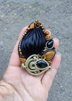 a hand holding a black and gold brooch with an animal on it's side