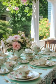 the table is set with tea cups, saucers and flowers in vases on it