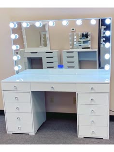 a white vanity with lights on it in front of a wall mounted mirror and drawers