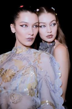 two models pose for the camera with their faces painted gold and silver, while wearing sheer clothing