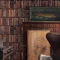 a chair in front of a book shelf filled with lots of books and a painting