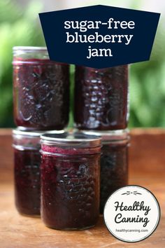 four jars filled with blueberry jam sitting on top of a wooden table