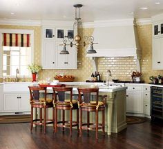 a kitchen with wooden floors and white cabinets, an island table surrounded by four stools