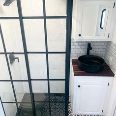 a bathroom with black and white tiles on the floor, shower stall door and sink