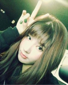 a woman with long brown hair and green nails making the peace sign while sitting in a car