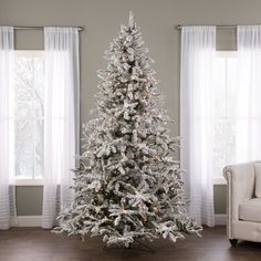 a white christmas tree in a living room next to a couch and window with curtains