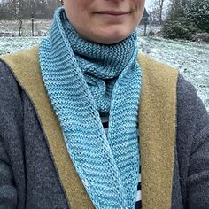 a woman wearing a knitted blue scarf and hat in the snow with trees behind her