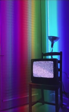 a television sitting on top of a wooden table in front of a rainbow colored wall