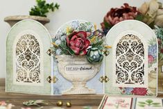 an ornate card holder with flowers in it on a table next to other cards and vases