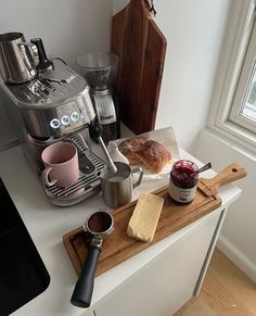 a coffee maker sitting on top of a counter next to some bread and jams