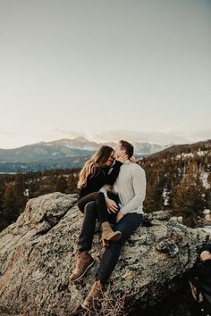 an engaged couple sitting on top of a mountain