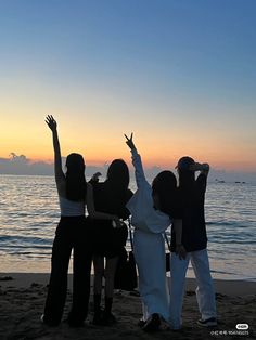 four people standing on the beach with their arms in the air and one person reaching up