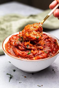 a hand holding a spoon full of meatballs with sauce in a small white bowl