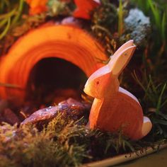 a toy rabbit sitting in the grass next to some rocks and plants with an orange light shining on it's head