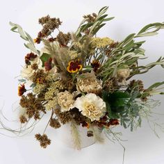 a vase filled with lots of different types of flowers and greenery on a white surface