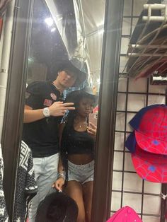 two people standing in front of a mirror with hats hanging on the wall behind them