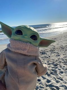 a baby yoda doll is standing on the beach