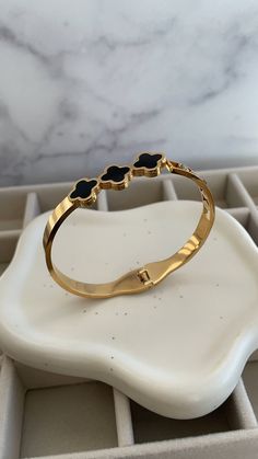 ✨Elevate your elegance with this exquisite gold bangle, a masterpiece that combines sophistication and sensuality. ✨Crafted with sleek gold and adorned with delicate black enamel clover motifs, this bracelet adds a touch of luxury to any ensemble. ✨The glimmering gold catches the light with every movement, while the bold clovers symbolize grace and allure. ✨A subtle diamond accent adds a hint of sparkle, making this piece the perfect companion for both day and night. Slip it on, and feel the confidence that only comes from wearing a truly captivating accessory. Black Gold-plated Bracelets, Elegant Black Enamel Bangle Cuff Bracelet, Elegant Black Enamel Cuff Bracelet Bangle Style, Elegant Black Enamel Cuff Bracelet, Elegant Black Bangle Gold Bracelet, Elegant Black Gold Bangle Bracelet, Elegant Black Bangle Bracelet, Luxury Metal Bracelets With Black Enamel, Elegant Black Enamel Bracelets As Gift