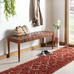 a wooden bench sitting in front of a window next to a rug and coat rack