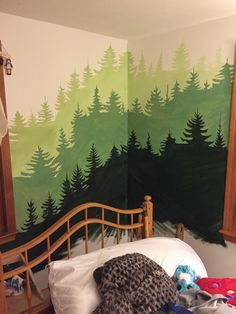 a bedroom with a forest mural painted on the wall and bed in front of it