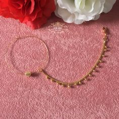 the gold bracelet is next to a flower on a pink surface with white flowers in the background