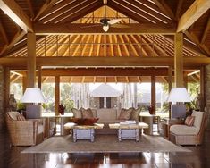 a living room filled with lots of furniture under a wooden roof covered in wicker