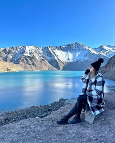 a woman sitting on top of a rock next to a lake with mountains in the background