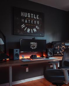 a desk with speakers and a computer on it in front of a poster that says hustle haters hiring