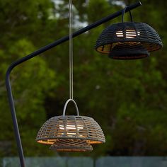 two lamps hanging from a metal pole in front of trees