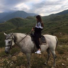 a woman riding on the back of a white horse down a hill covered in grass