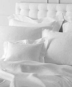 a bed with white sheets and pillows on top of it, in black and white