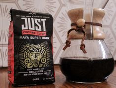 a bag of just coffee next to a pour - over on a wooden countertop