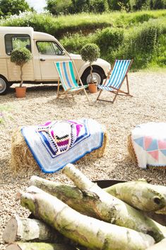 two lawn chairs sitting on top of a gravel field next to a parked van and hay bales