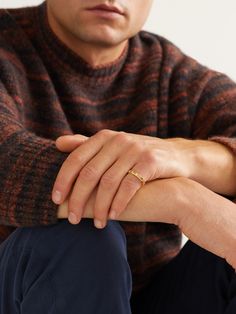 a man sitting on the ground with his hand resting on his knee wearing a gold ring