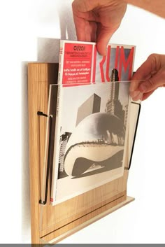 a person is holding up a magazine in front of a wooden frame that holds photos