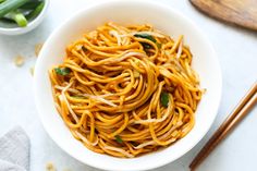 a white bowl filled with noodles next to chopsticks