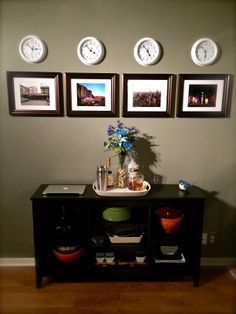 there are three clocks on the wall above a table with vases and bowls in front of it