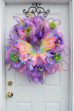 a purple mesh wreath with butterflies and flowers on the front door to a white house