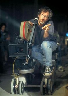 a man sitting on top of a camera in front of a projector with his hand pointing at the camera