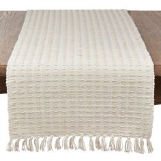 a white table runner with tassels on the edge and wood flooring behind it