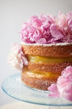 a three layer cake with pink flowers on top and frosting in the middle, sitting on a glass plate