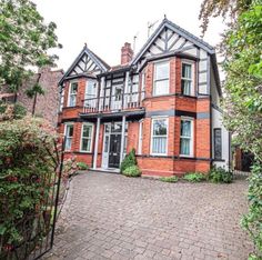 a large brick house with lots of windows on the front and side of it, surrounded by greenery