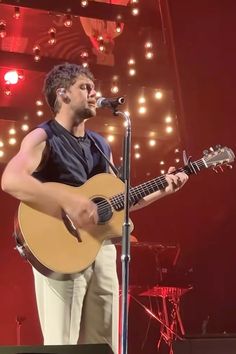 a man holding a guitar while standing in front of a microphone on top of a stage