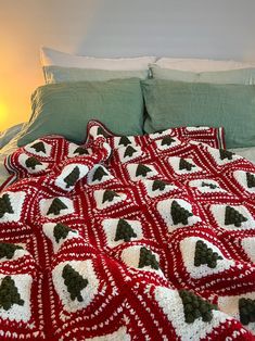 a red and white crocheted christmas blanket on a bed with green pillow cases